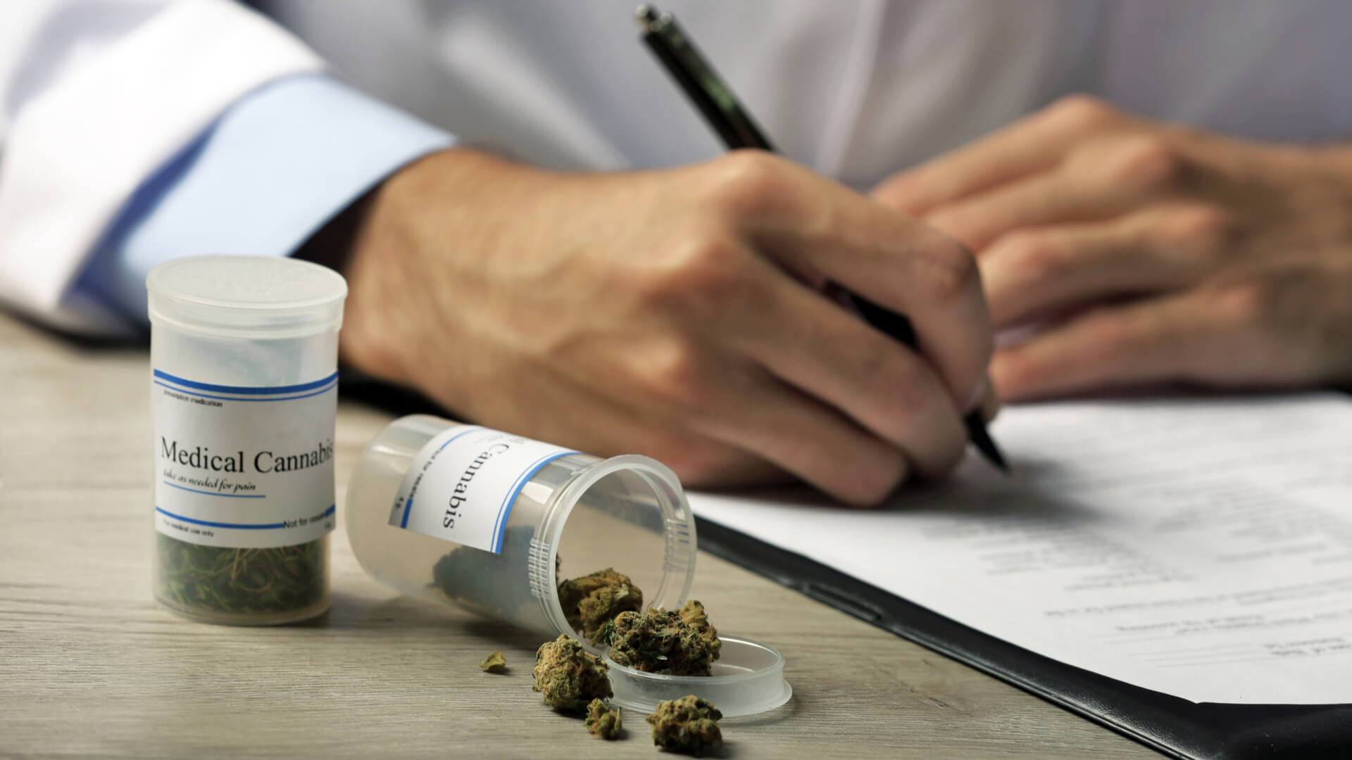 Doctor writing on prescription blank with a bottle of medical cannabis next to him